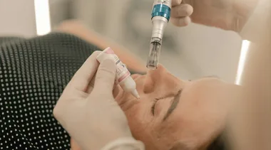 Mãos com luva aplicando máscara facial no rosto de uma cliente